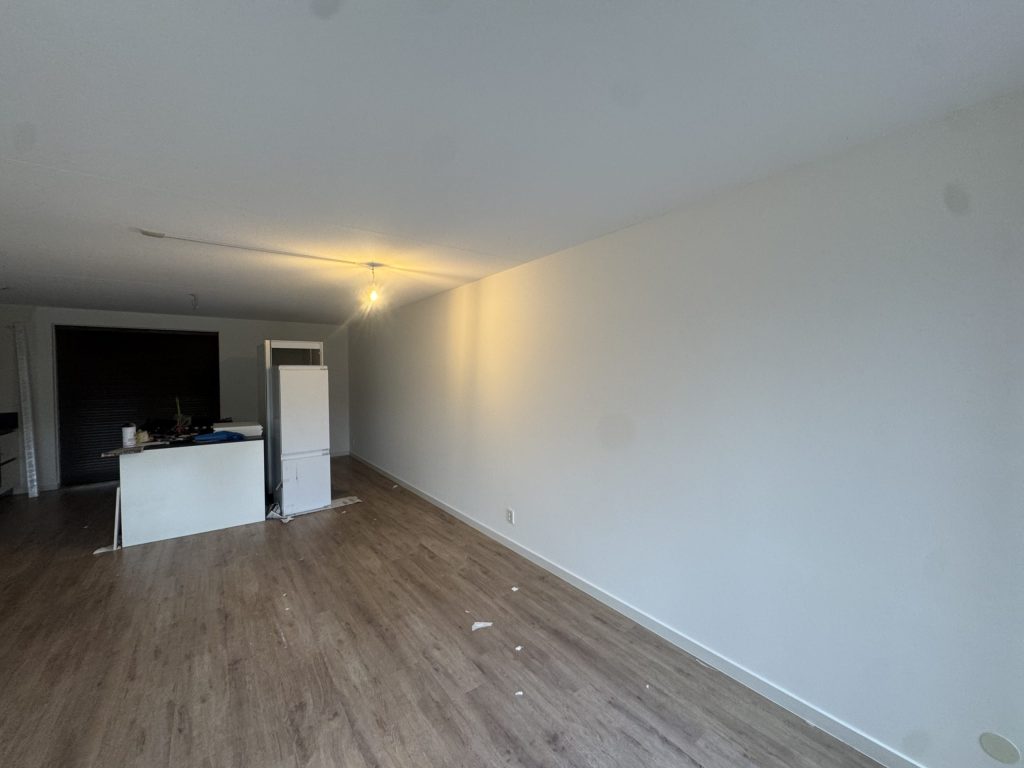 Lange witte wand in een woonkamer met open keuken en laminaatvloer