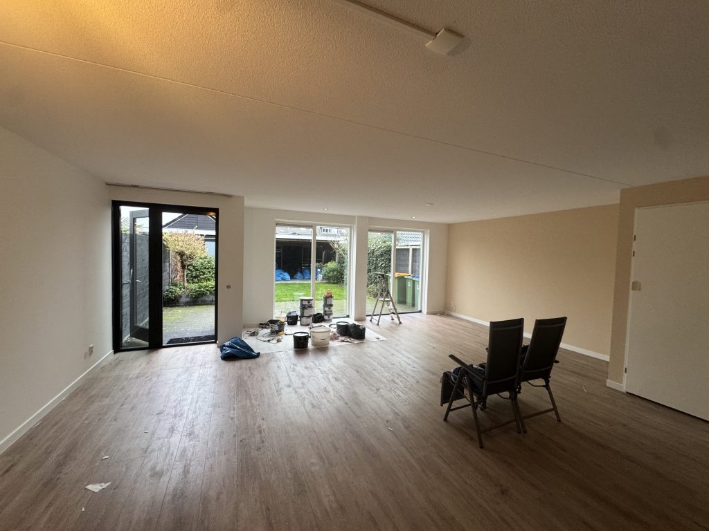 Ruime woonkamer met tuindeuren, een houten vloer en verfemmers, klaar voor de laatste sauslaag